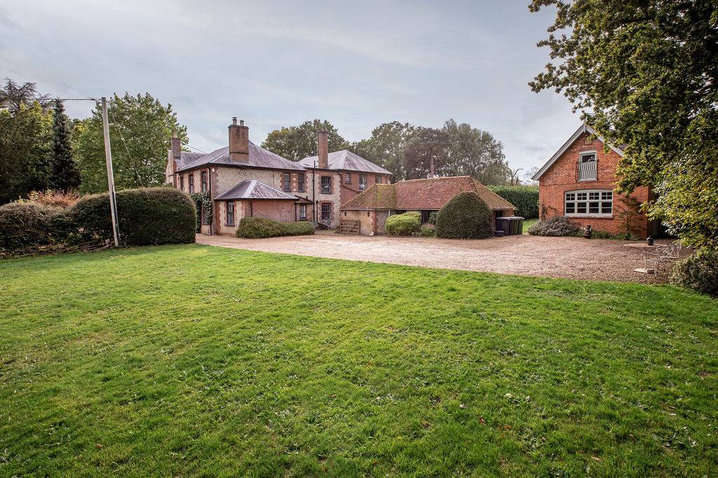 Wide exterior view of a countryside home with landscaped gardens, mature trees and traditional outbuildings in Liss, Hampshire GU33 – available through Love Locations.