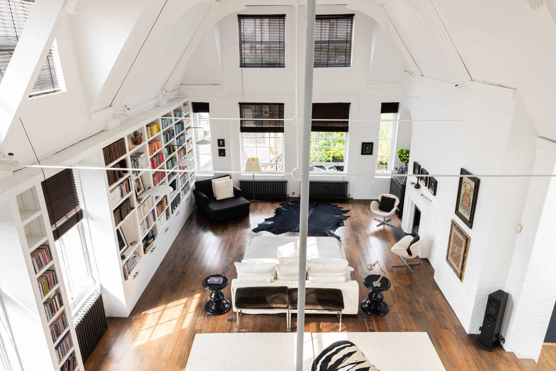High-angle mezzanine view looking down over a vaulted white loft studio room with dark wood floors and butterfly rug, Love Locations SW11.