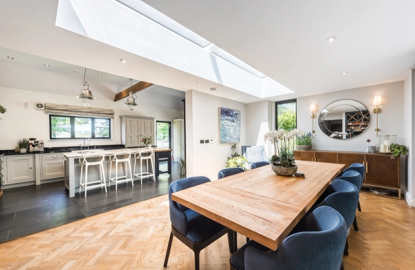 High-end dining room setup with a rustic wooden table and blue velvet chairs under a skylight window, Love Locations CM3.