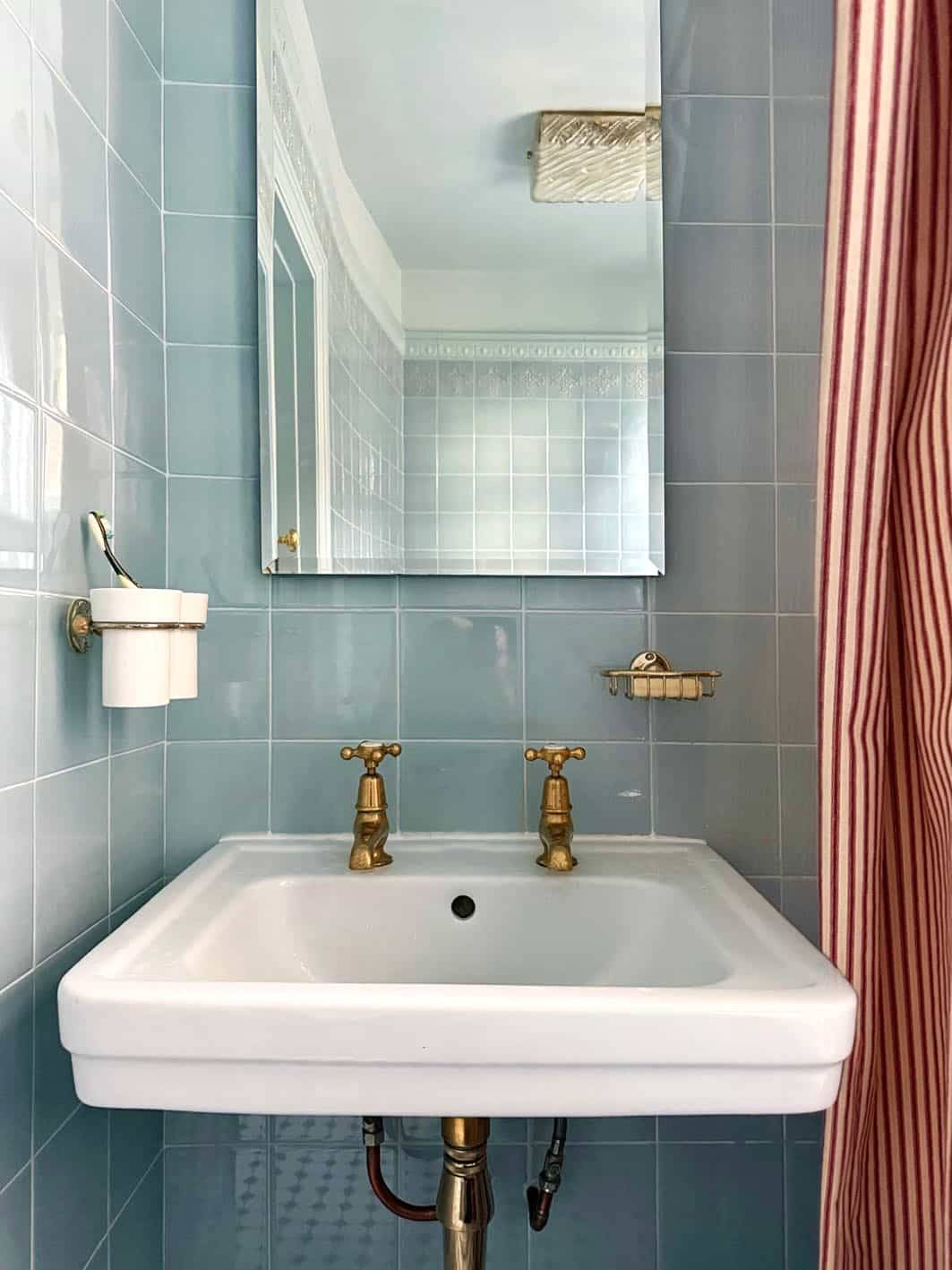 Retro bathroom sink with white pedestal, brass taps, and blue wall tiles, Love Locations N13.