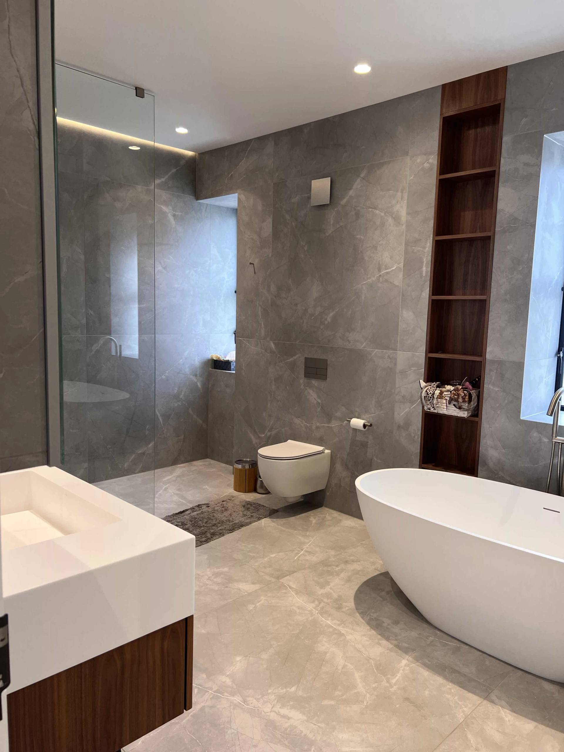 Contemporary grey tiled bathroom with a freestanding tub, floating white sink, and walk-in shower enclosure, Love Locations.