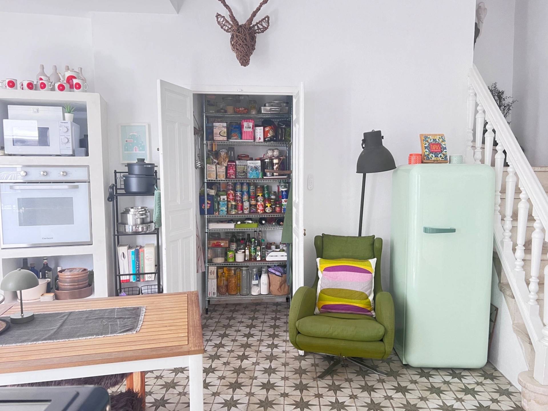 Kitchen pantry nook location featuring an olive green armchair, retro SMEG refrigerator, and open wall storage in Jimena de la Frontera through Love Locations.