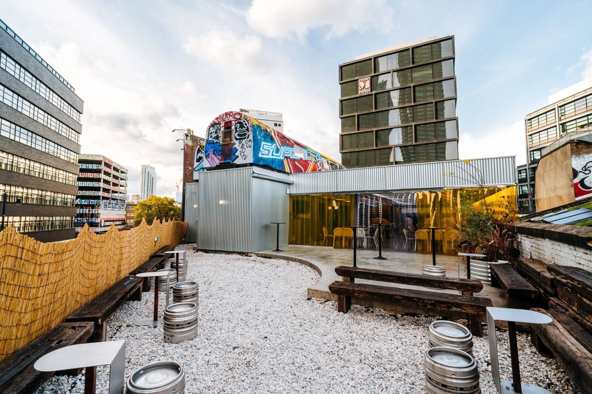 Outdoor rooftop courtyard venue in Hackney EC2A through Love Locations, featuring gravel landscaping, outdoor bench seating, and repurposed vintage train carriages.