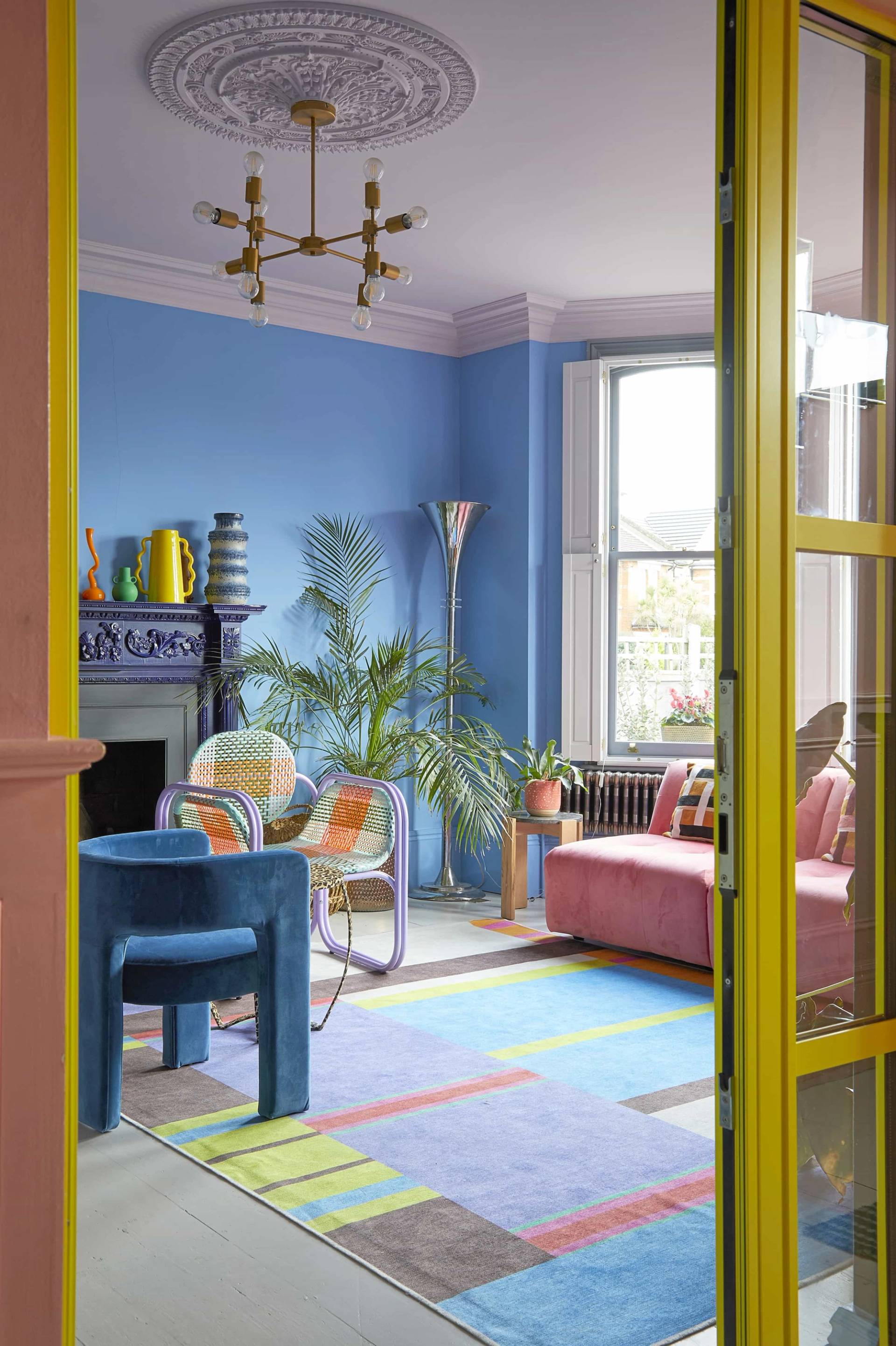 Looking through yellow door frames into a periwinkle blue reception room with colorful patterned furniture, Love Locations SE6.