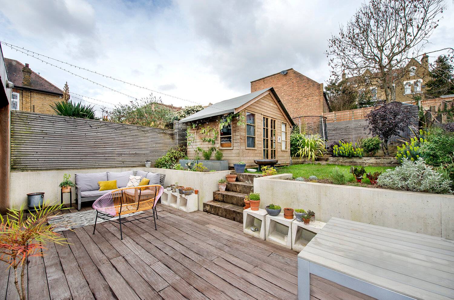 Landscaped garden patio in Forest Hill, SE23 with timber decking, concrete steps, outdoor seating, and a standalone garden studio house, Love Locations.