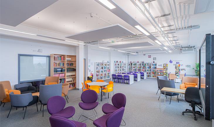  Modern school library and breakout lounge film location featuring purple tub armchairs, circular tables, and bookshelf units from Love Locations.