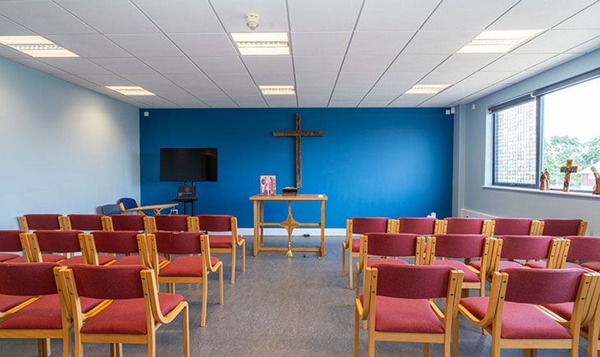 Love Locations school chapel location South East London SE2: Intimate prayer hall featuring a vibrant blue feature wall, wooden cross, and red cushioned chairs, ideal for indie films and TV drama scenes.