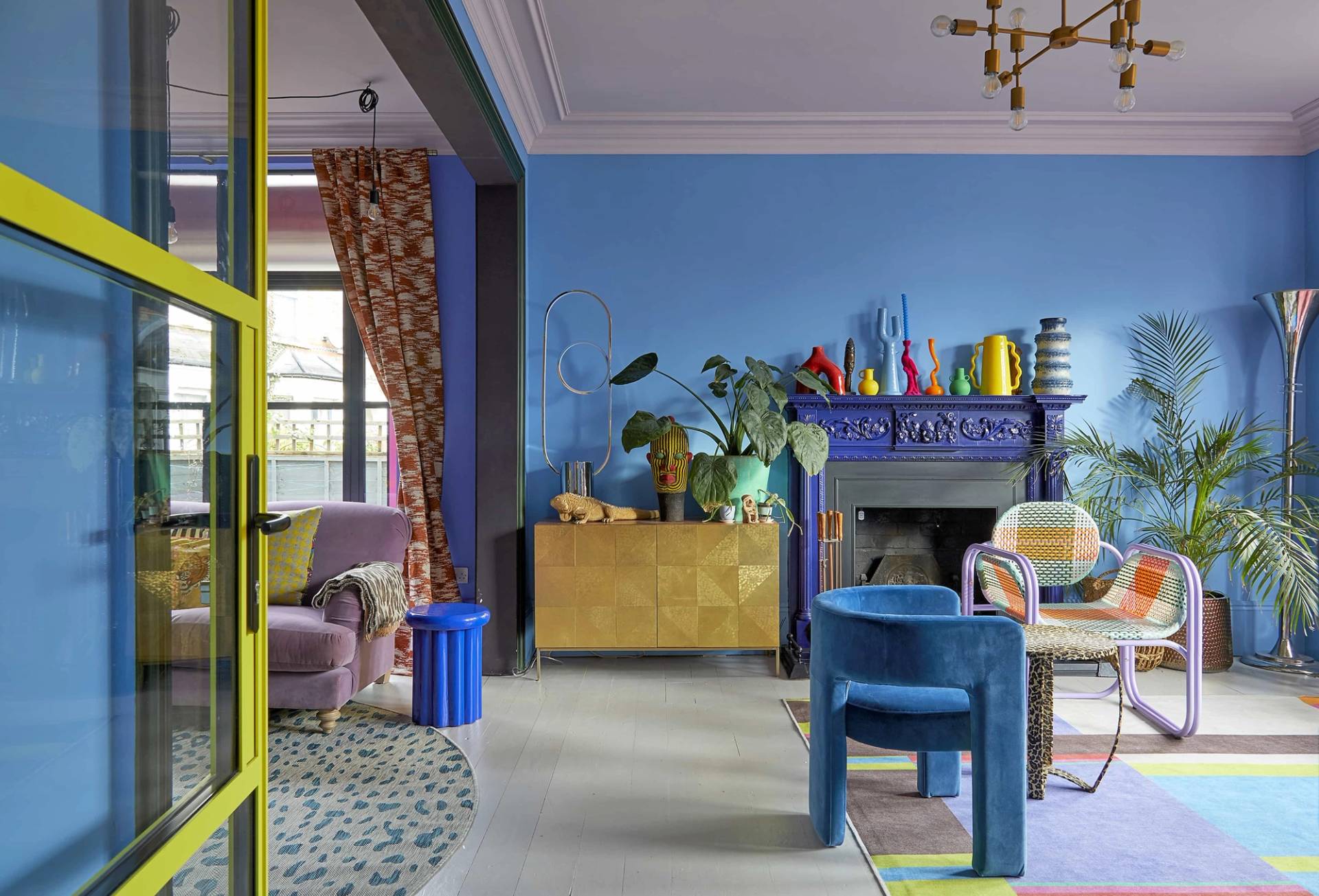 Vibrant blue living room with a gold credenza, purple armchairs, and yellow window frames in SE6, Love Locations Catford.