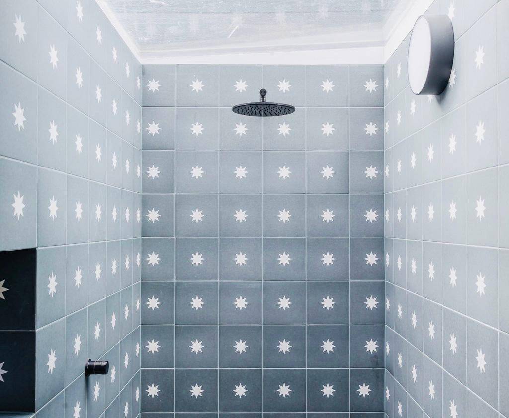 Walk-in shower enclosure wrapped in grey square tiles with a black overhead rain shower head, Love Locations TW11.
