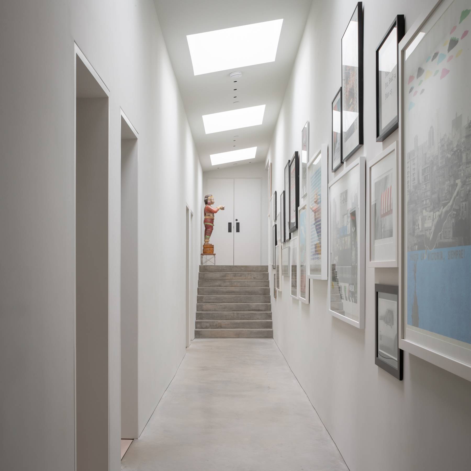 Skylit gallery hallway with polished concrete flooring and white walls displaying framed art prints, Love Locations BN3.