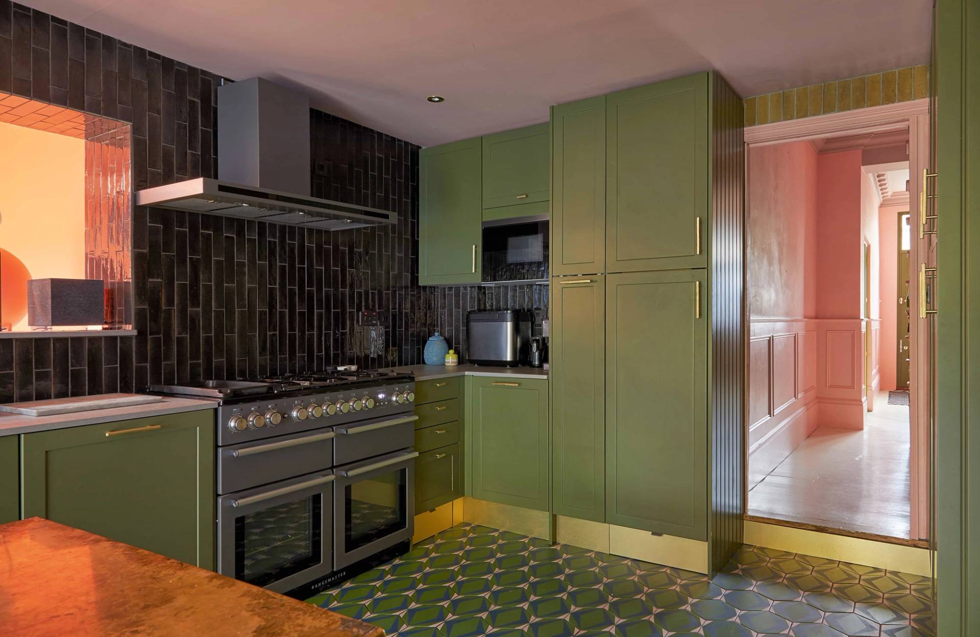 Olive green kitchen setup with a dark tiled splashback, integrated range cooker, and brass taps, Love Locations SE6.