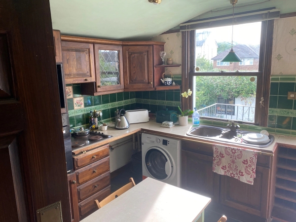 Authentic suburban kitchen setup with a washing machine, wooden counter units, and a large window overlooking the rear yard, Love Locations.