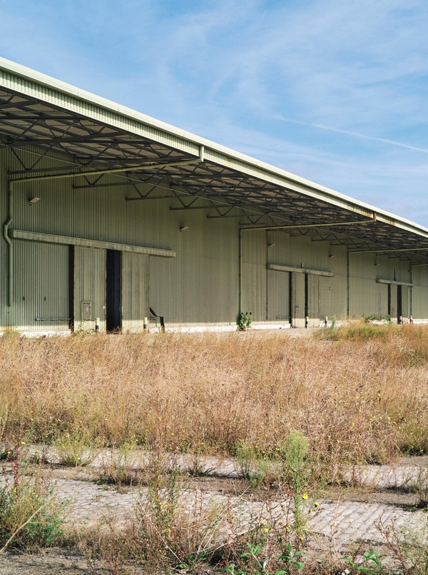Derelict green industrial warehouse exterior surrounded by overgrown wild grass, a unique cinematic backdrop for post-apocalyptic film sets, Love Locations.