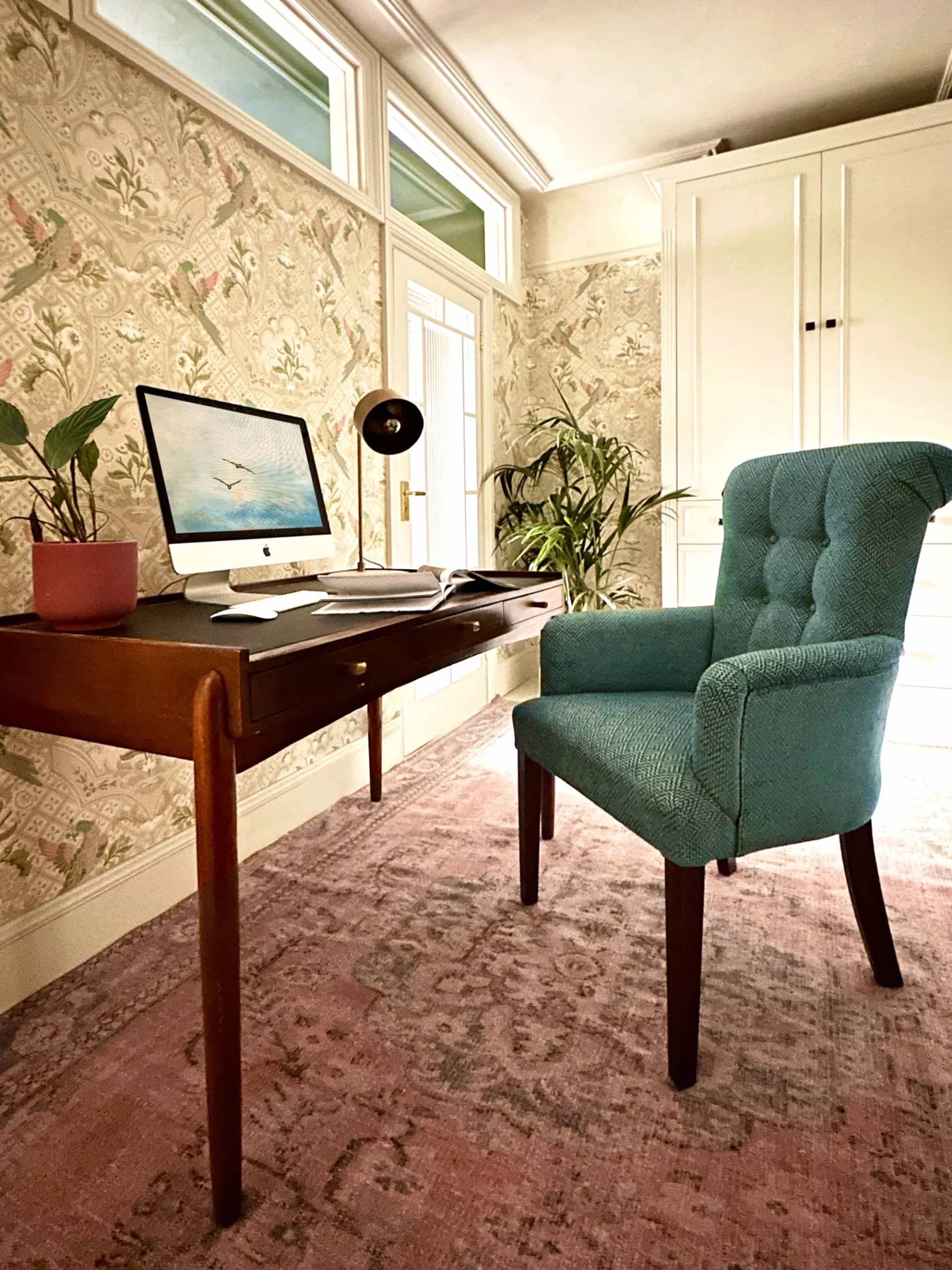 Period study desk setup with green button-tufted armchair, laptop, and sunlit window, Love Locations N13.