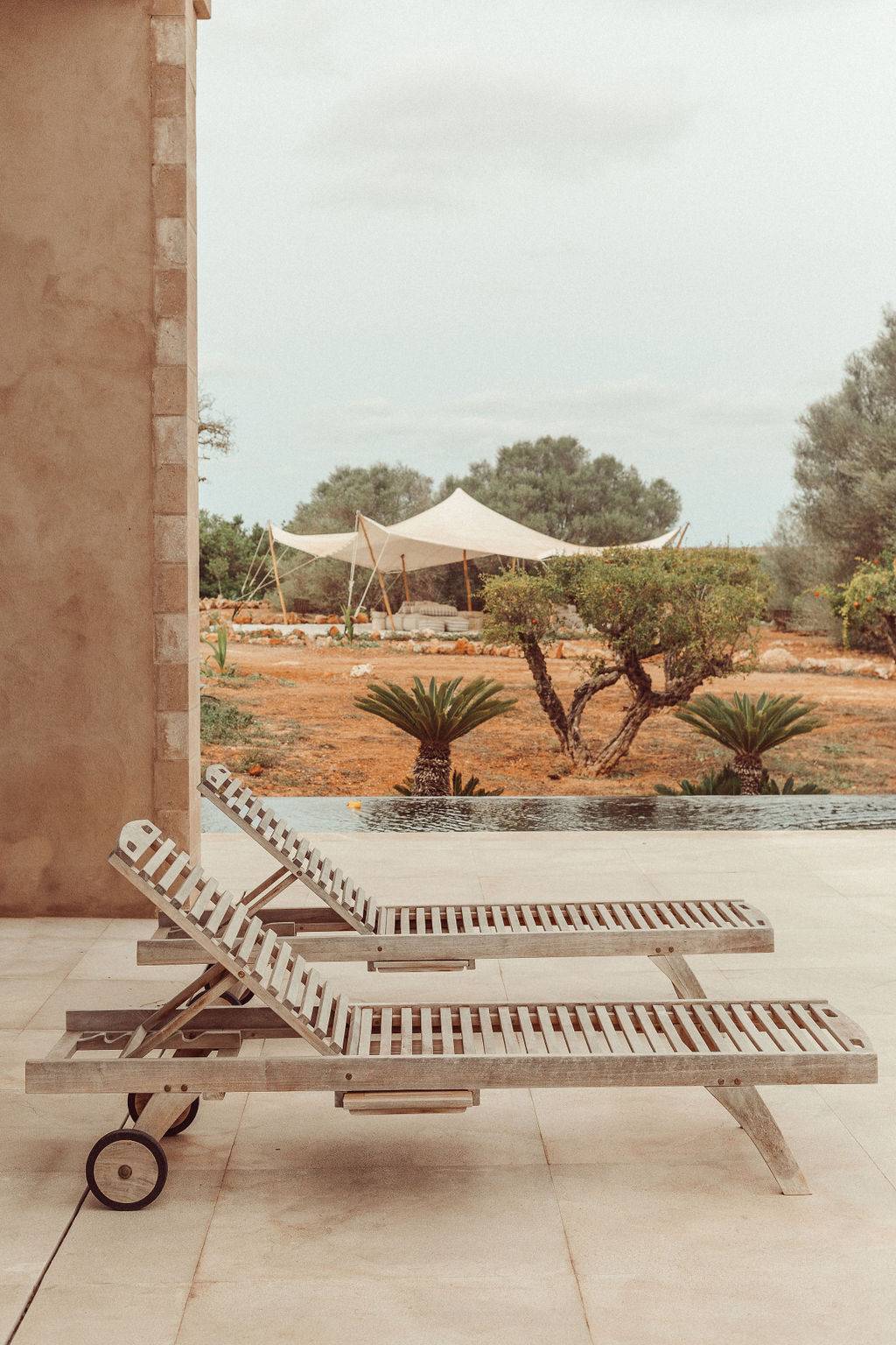 Wooden sun loungers set on a stone poolside terrace beside an outdoor canopy bed, Love Locations 07630.