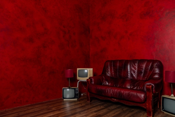 Dramatic red texture-painted studio set featuring a red leather sofa and stack of vintage CRT television sets, Love Locations N15.