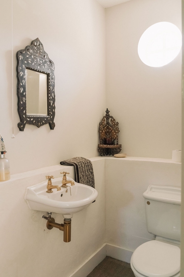 Compact guest cloakroom toilet featuring a white basin, traditional wall mirror, and brass fixtures, Love Locations.