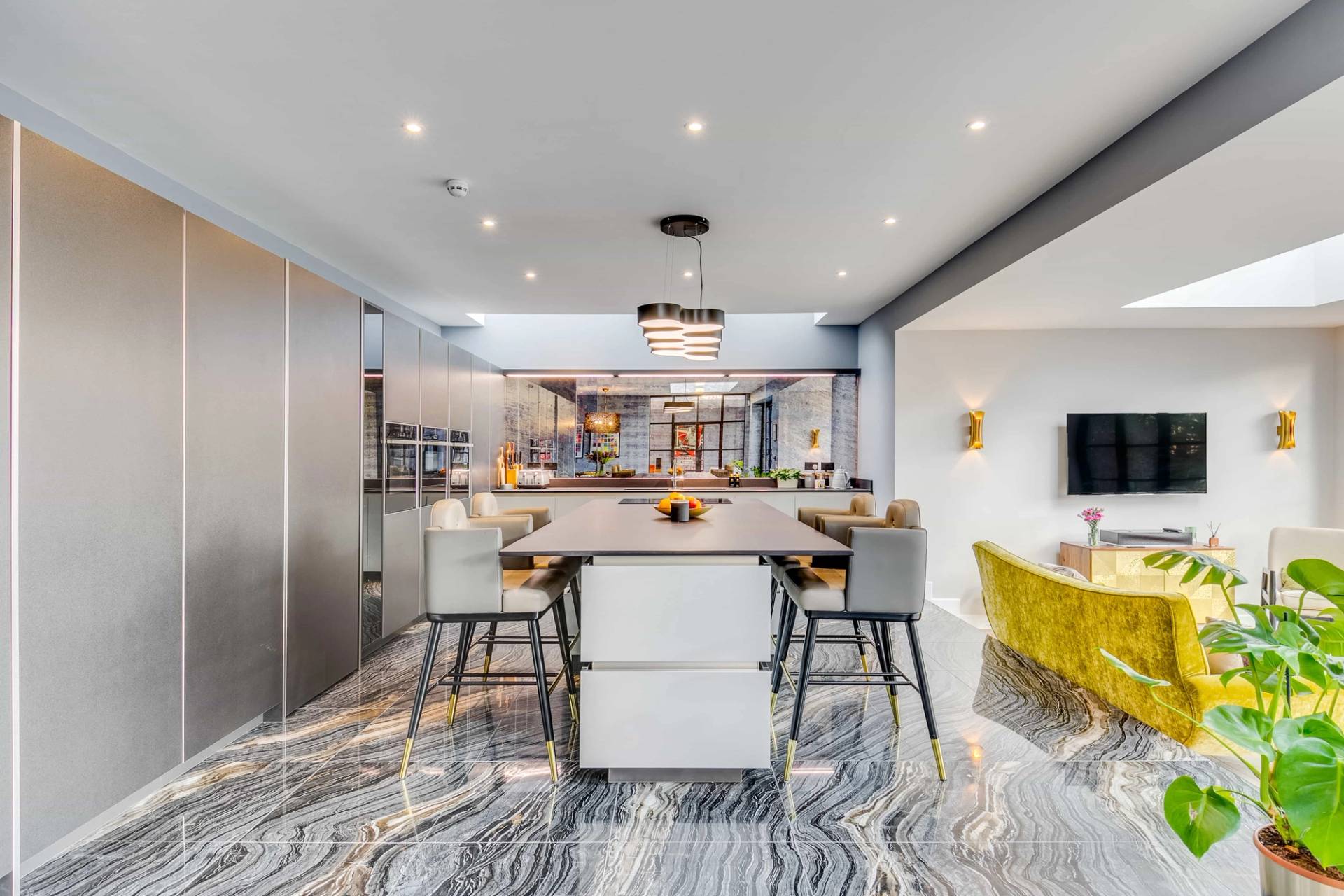 Modern kitchen suite featuring a large island unit, grey bar chairs, dark marble flooring, and crittall garden doors, Love Locations CB2.