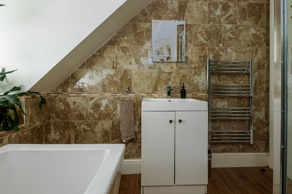 Character bathroom with sloping ceiling and stone-effect walls at Love Locations property in Liss, Hampshire GU33. Freestanding bath beneath vaulted ceiling at Love Locati