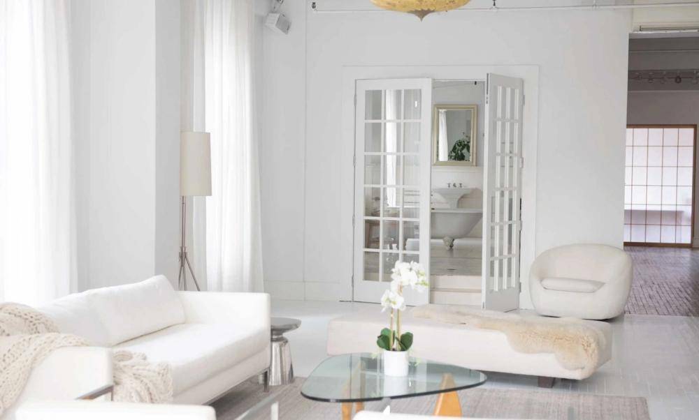 Open interior view looking past a minimalist living room toward classic white double doors in a New York loft studio, Love Locations.