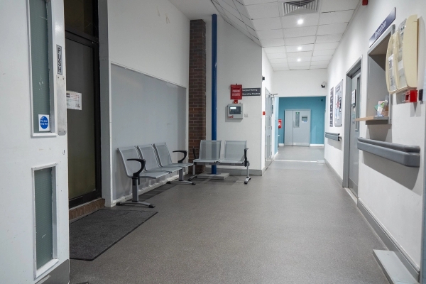 Bright hospital corridor with metal waiting chairs, linoleum flooring, and white walls, Love Locations UB4.