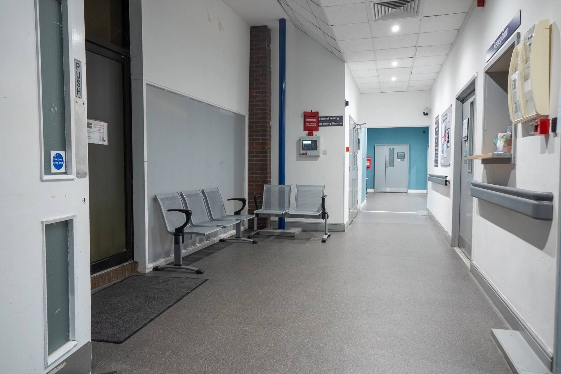Bright hospital corridor with metal waiting chairs, linoleum flooring, and white walls, Love Locations UB4.
