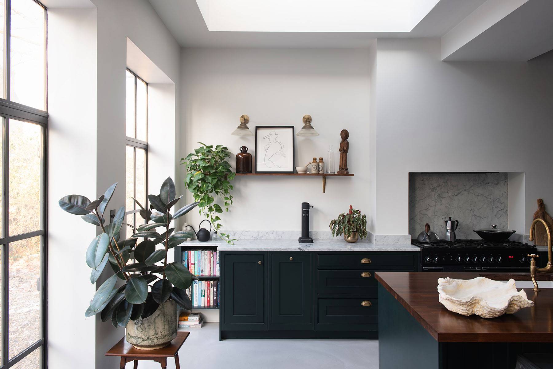 Symmetrical shot of dark green kitchen cabinets with open wood shelving, marble backsplash, and potted plants, Love Locations SW16.