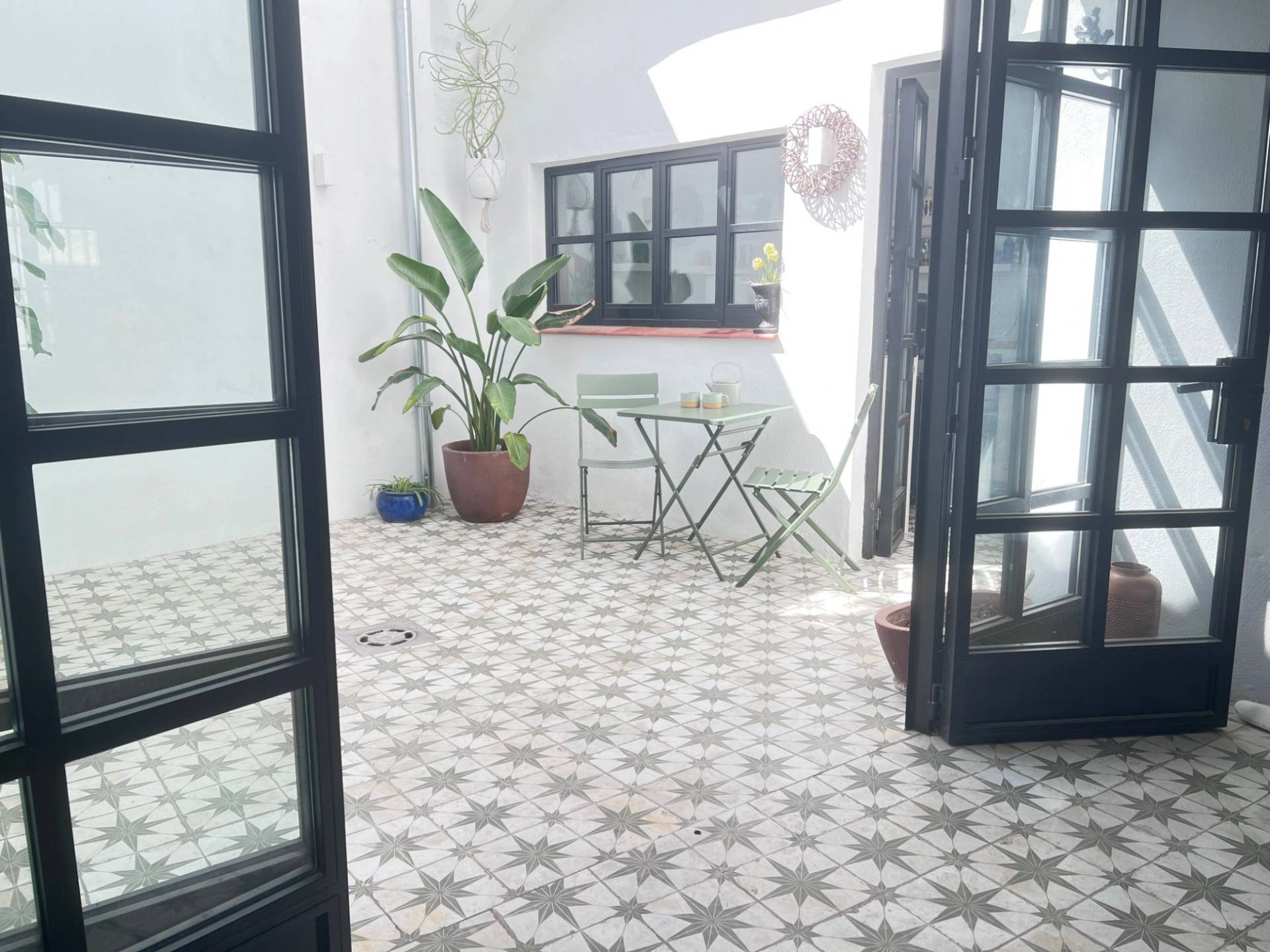 Private internal courtyard patio film location in Jimena de la Frontera through Love Locations, showcasing black crittall-style French doors, patterned tile flooring, and potted plants.