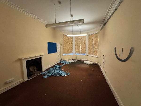Large derelict classroom or hall with blue plastic scrap debris strewn across a dark red carpet, managed by Love Locations.