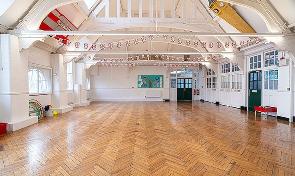 Grand double-height school hall featuring exposed timber roof trusses and green double doors, available for media hire via Love Locations.
