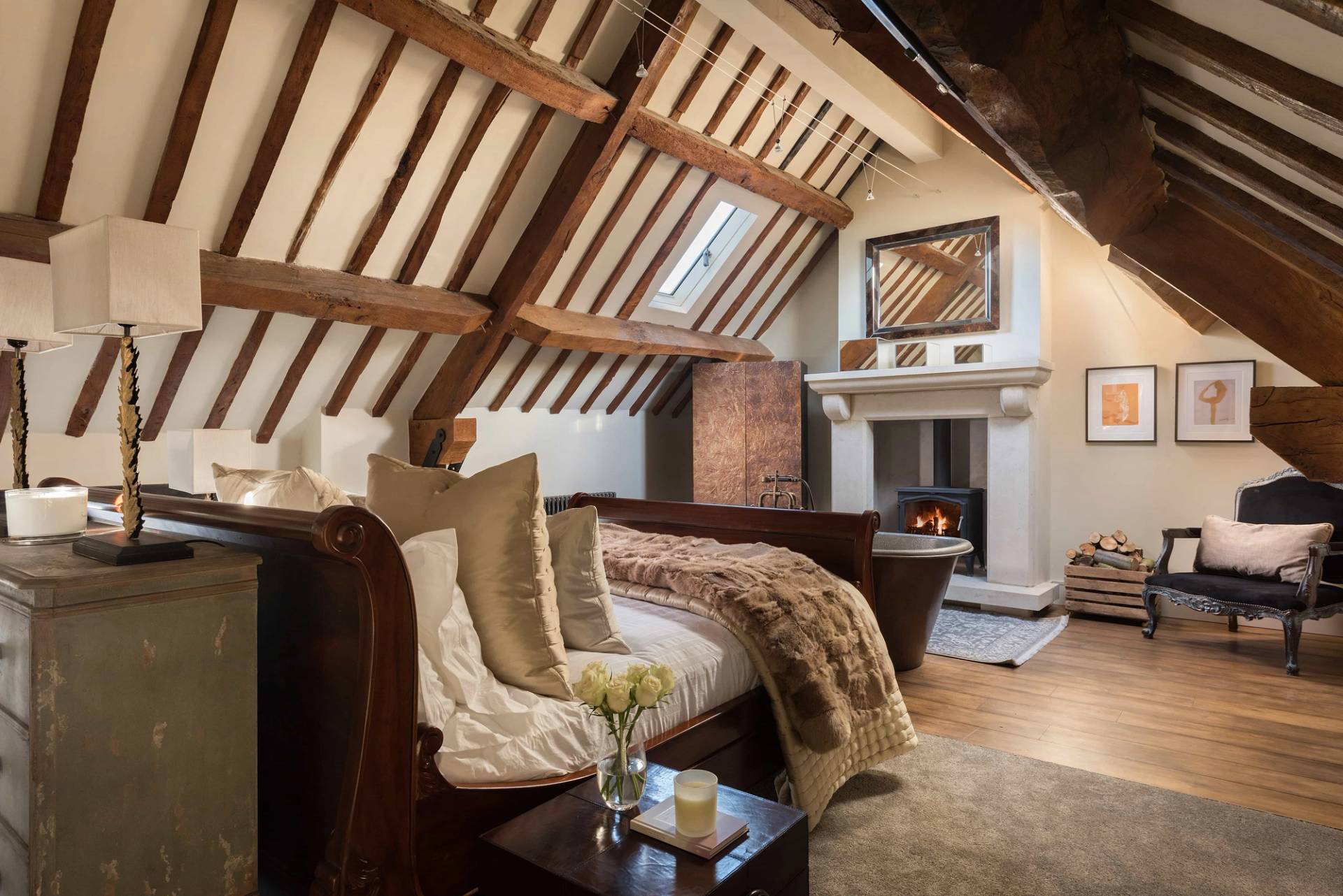 Vaulted attic bedroom shoot location with exposed dark timber roof trusses and a rustic stone fireplace via Love Locations.
