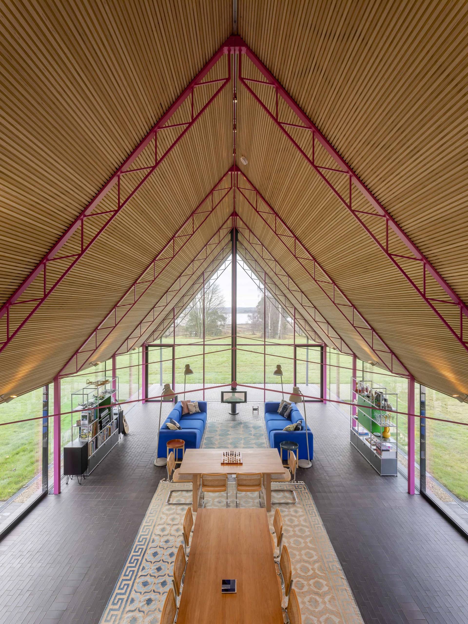 High-angle perspective looking down a vaulted glass hall with pink steel trusses and blue sectional sofa seating, Love Locations IP17.