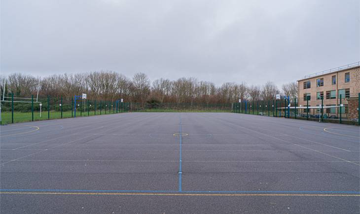 Expansive tarmac school playground shoot space with painted sports court markings and tree-lined perimeter via Love Locations.