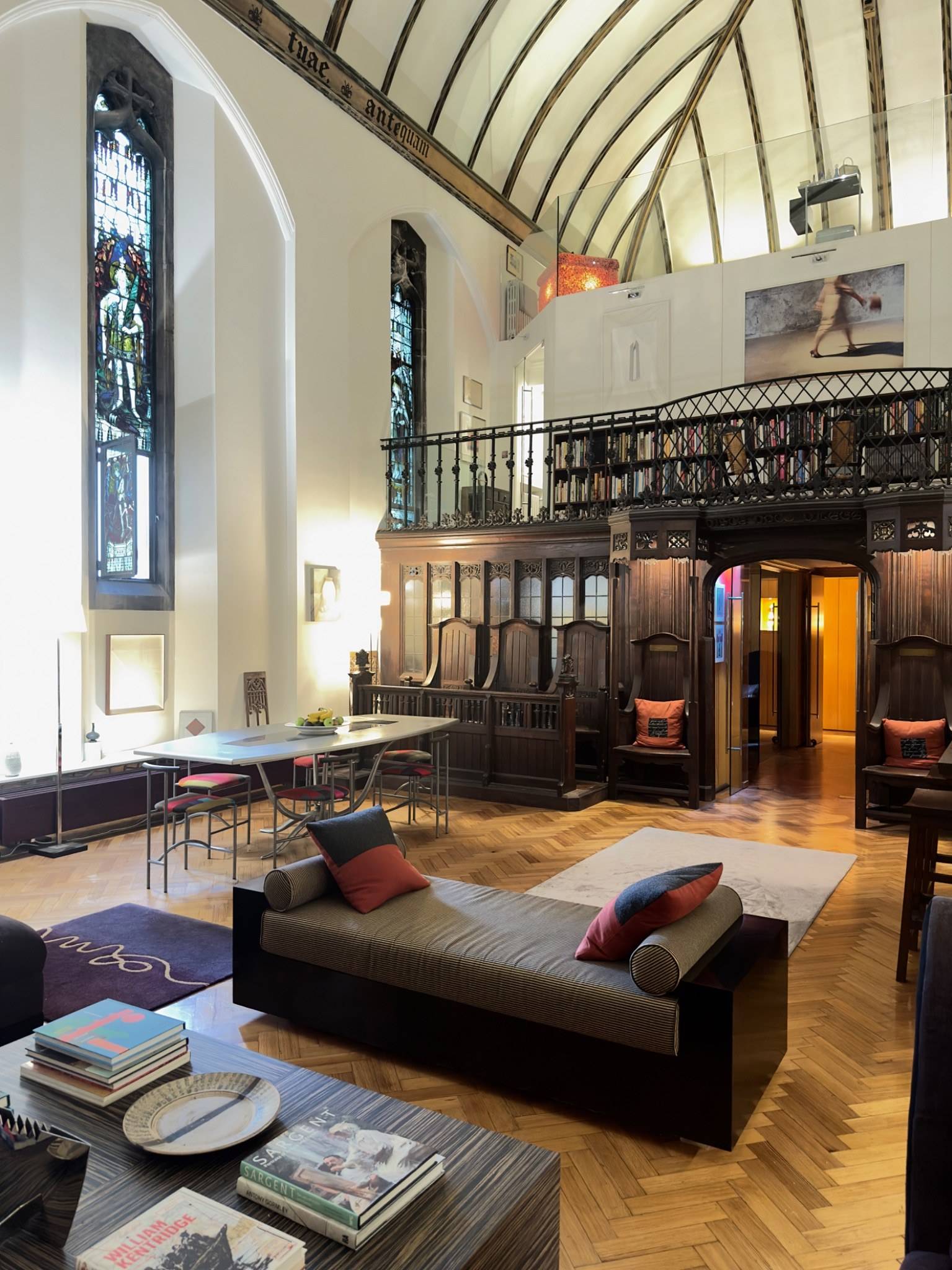 Spacious nave interior featuring low-slung contemporary sofas, polished parquet wood floor, and high gothic windows in Oval SE5 via Love Locations.