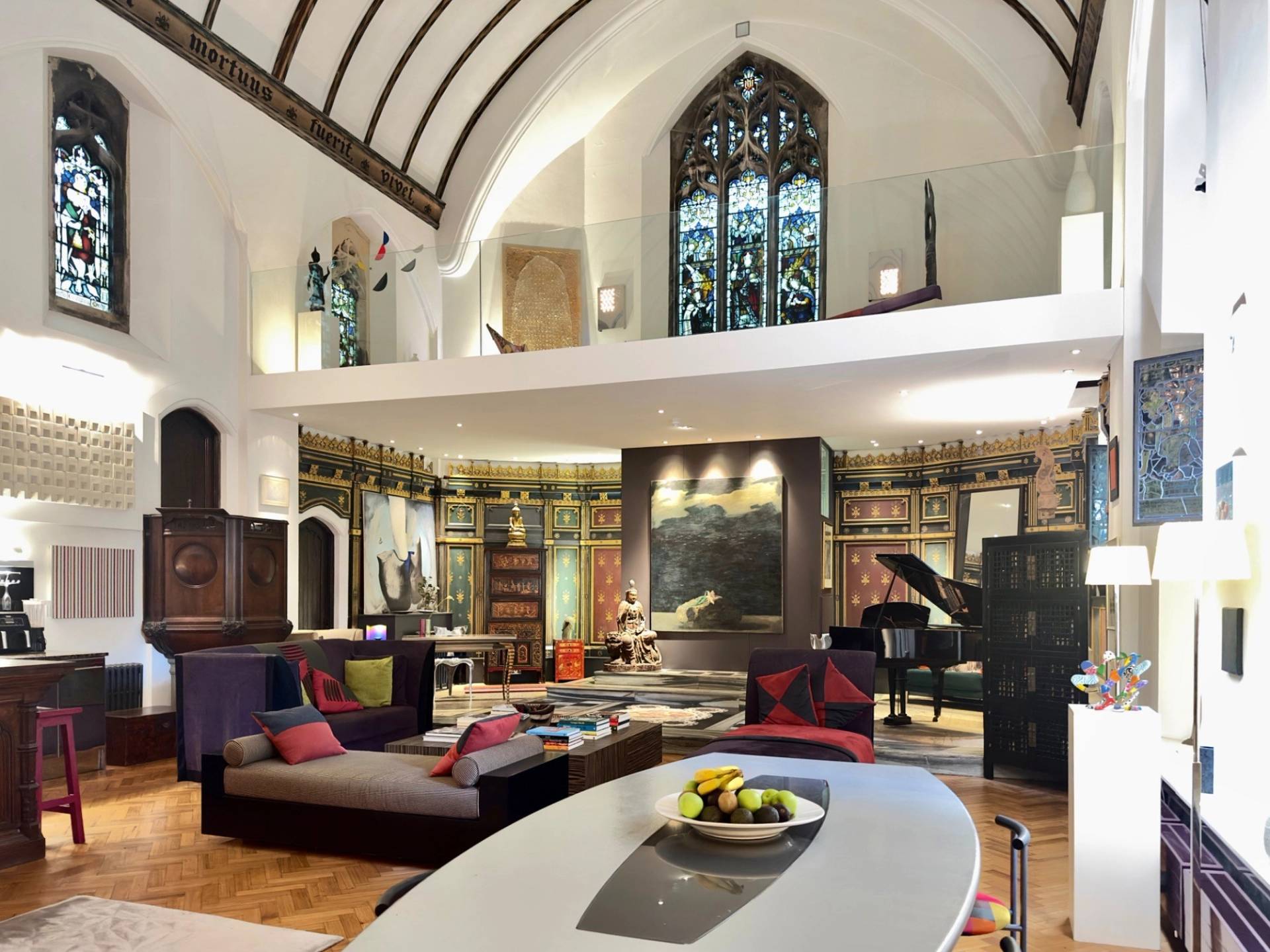 Double-height vaulted ceiling living area in a converted chapel film location in Oval SE5 from Love Locations, featuring grand arched windows, mezzanine gallery, and plush modular seating.