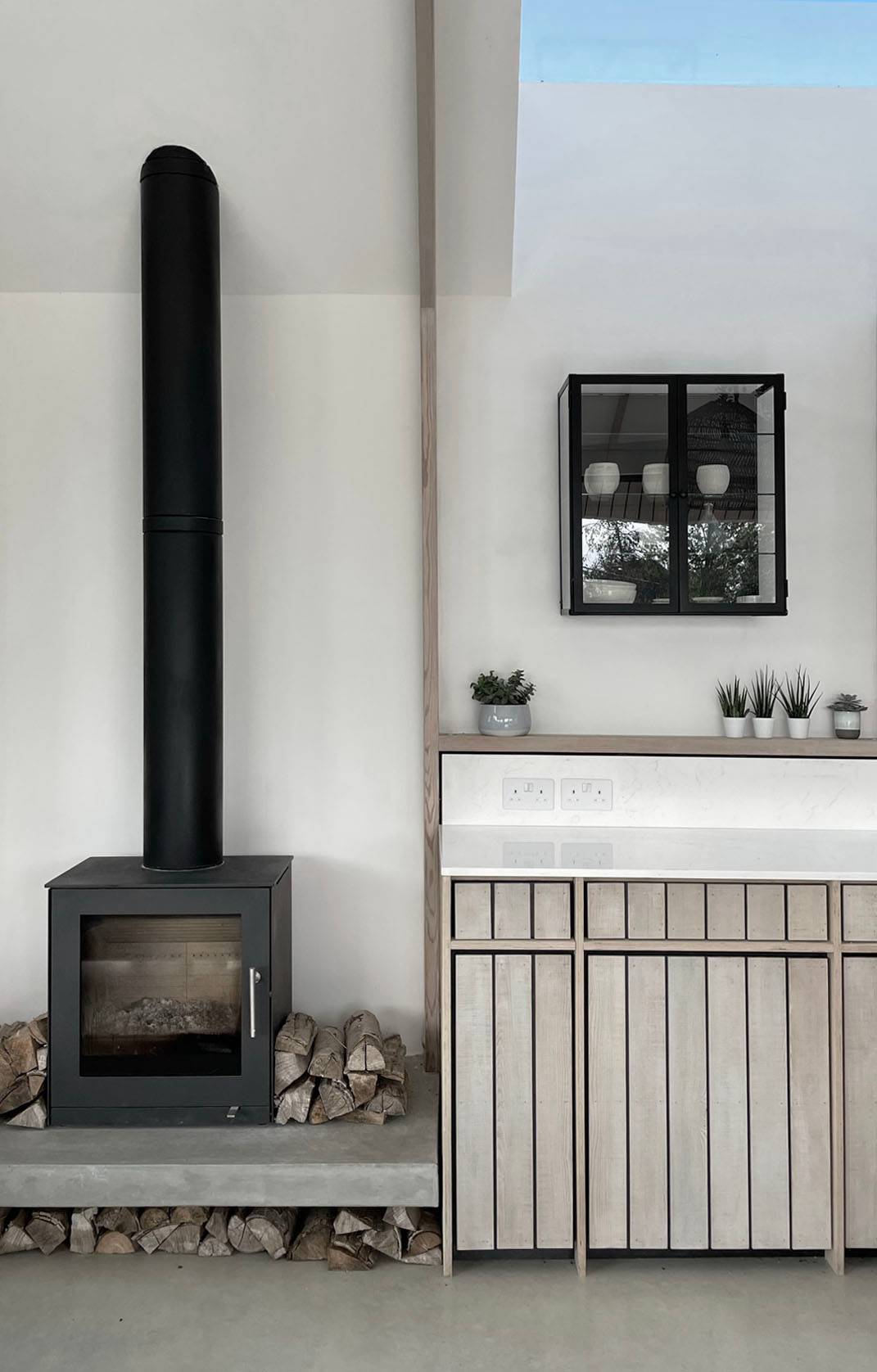 Cozy fireplace alcove with a black wood-burning stove and bespoke slatted timber cabinetry storage, Love Locations.