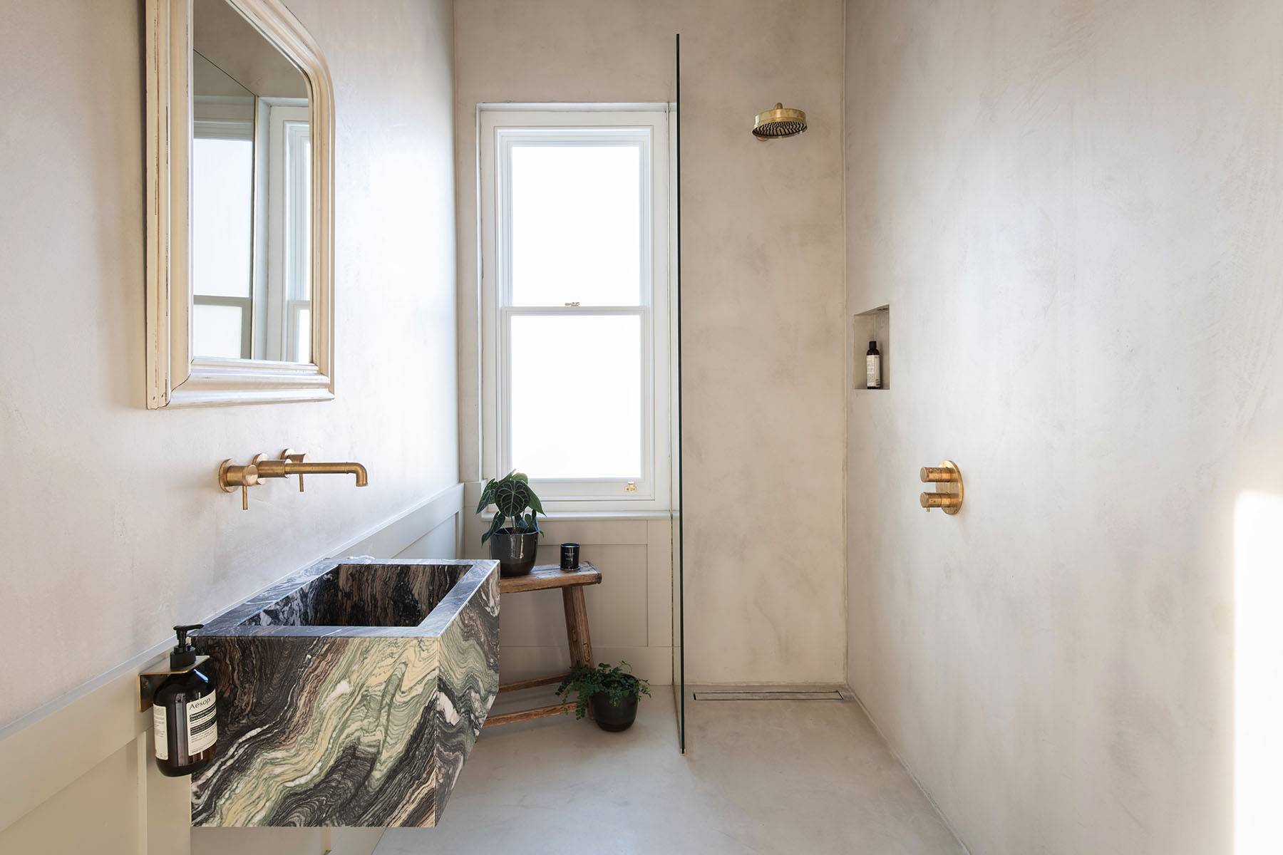 Ensuite bathroom transition with a dramatic green-veined marble sink block, brass wall taps, and cream wabi-sabi walls, Love Locations SW16.