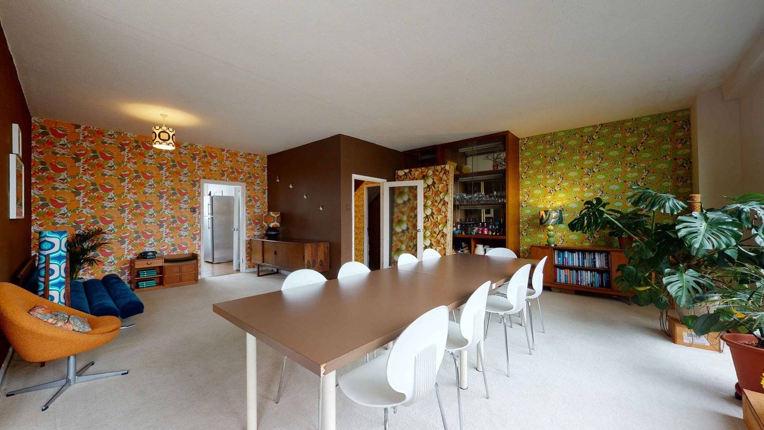 Spacious mid-century dining space with brown painted accent walls, floral 70s wallpaper, and white dining chairs, Love Locations SW16.