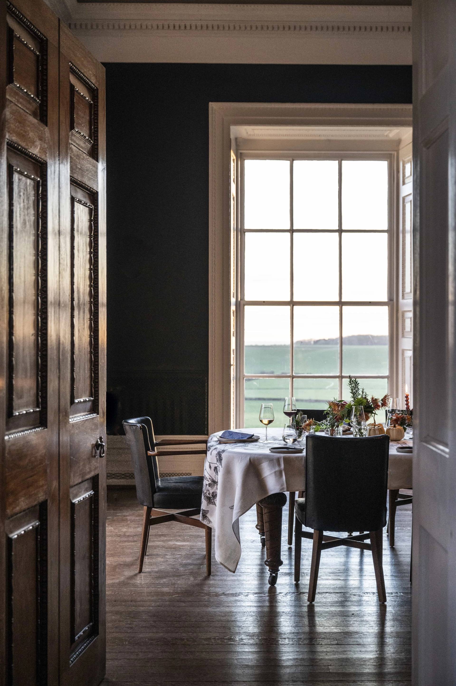 Close-up detail of a formal set dining table positioned beside a tall sash window with dark wood shutters, Love Locations LE7.