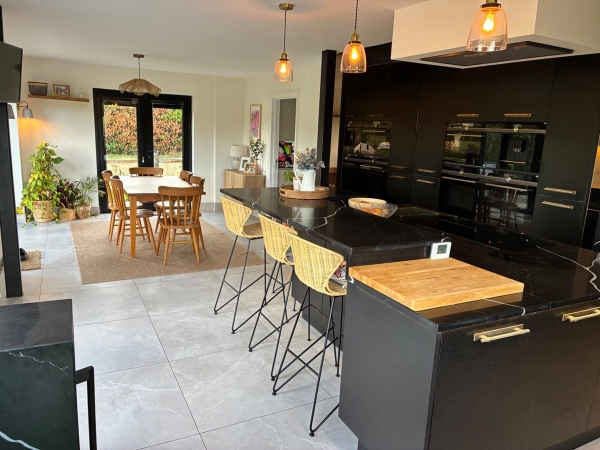 Light-filled kitchen and casual seating area in Essex CM4 via Love Locations, displaying black cabinetry, light tiled flooring, and modern bar seating.