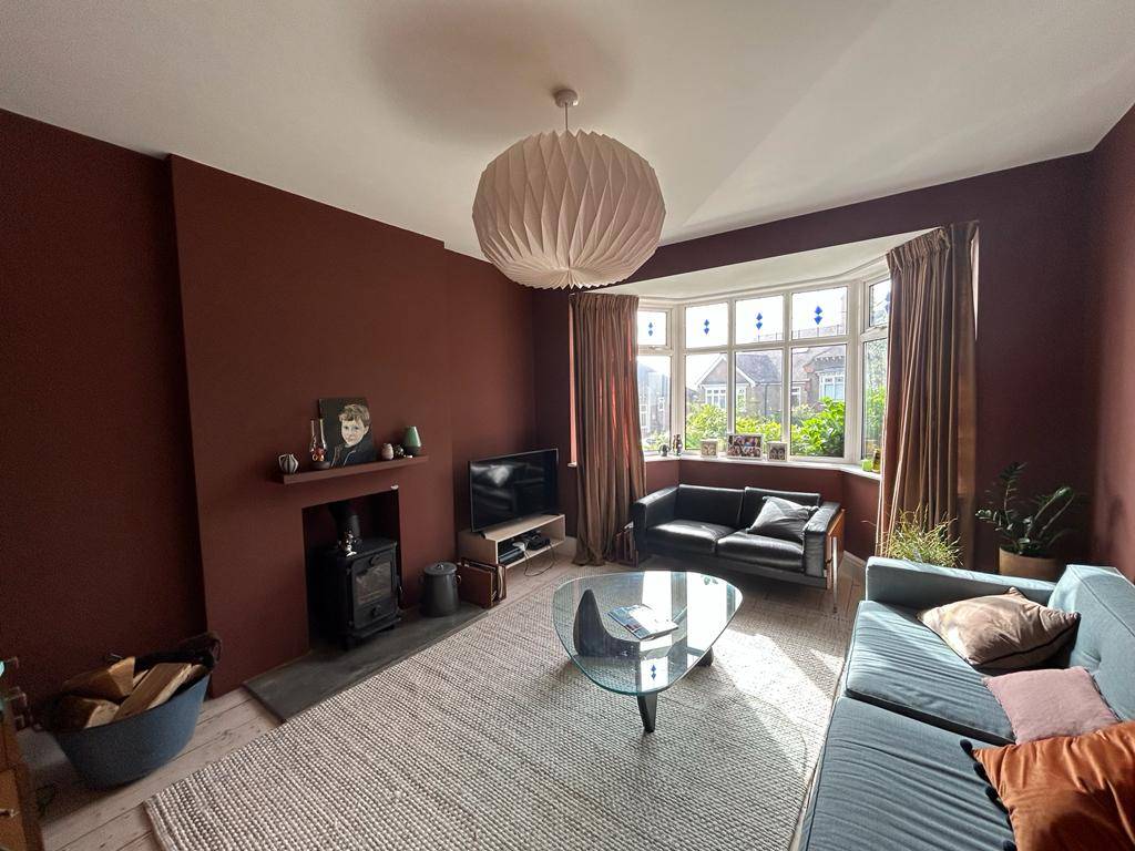 Cozy period reception room with rich terracotta red accent wall, dark brown leather sofa, and bay window light, Love Locations Forest Hill.