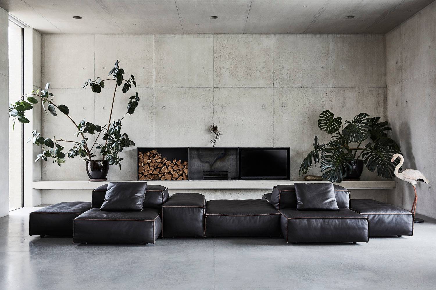 Brutalist modern shoot location in Oval, SW8 featuring board-marked raw concrete walls, low-profile black leather modular sofa, polished concrete floor, and integrated log storage, ideal for high-fashion editorial campaigns via Love Locations.