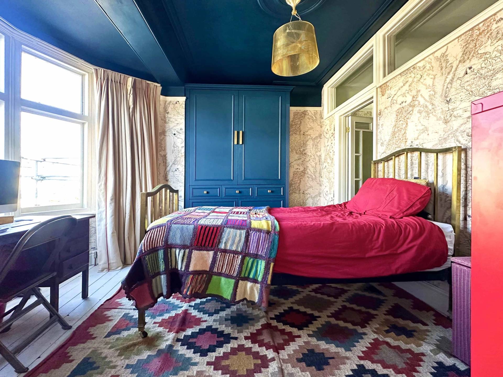Vibrant bedroom featuring a dark blue ceiling, patterned wallpaper, red bedspread, and blue wardrobe, Love Locations N13.