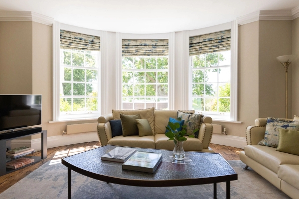 Love Locations elegant bay window reception room Steyning: Sprawling lounge area featuring a curved window alcove, cream sofa, and abundant natural light, ideal for tracking shots and fashion editorials.
