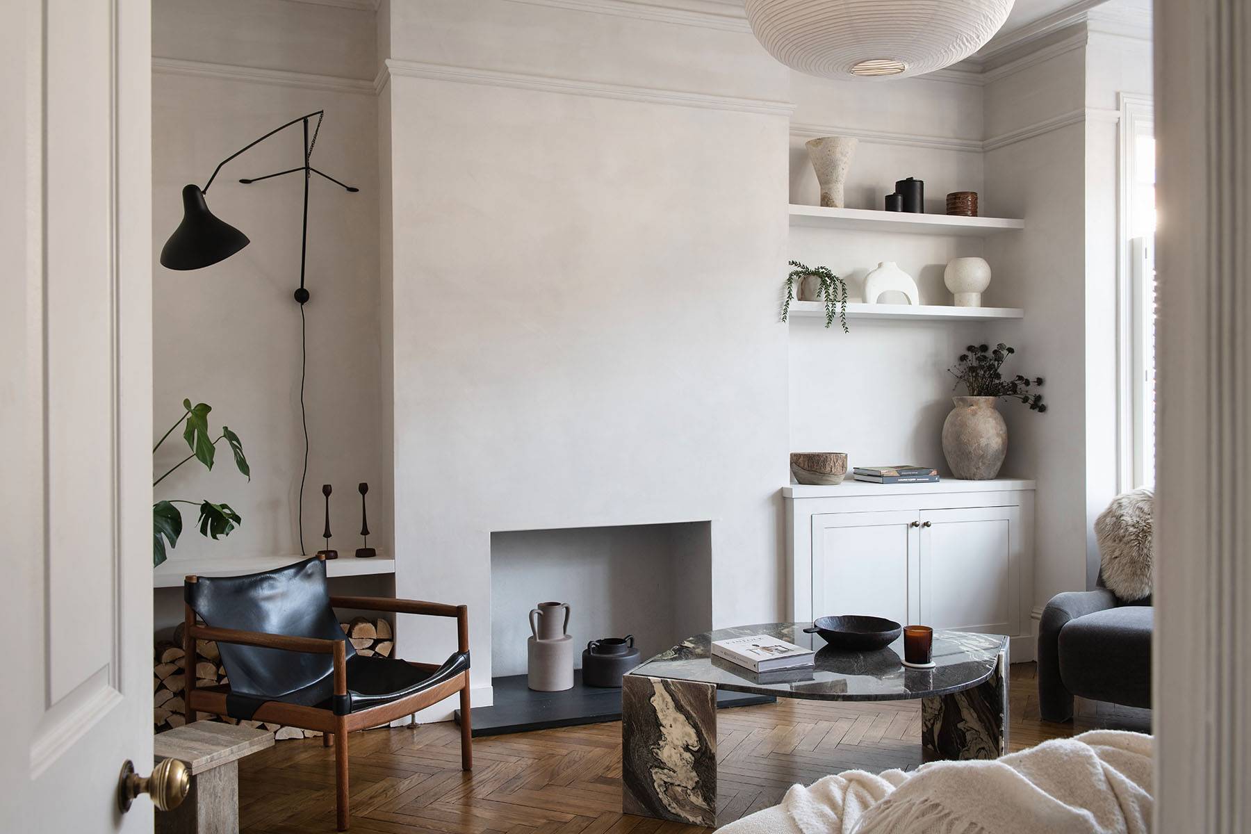 Minimalist plaster reception room with recessed fireplace alcove, dark wood armchair, and organic stone coffee table, Love Locations SW16.