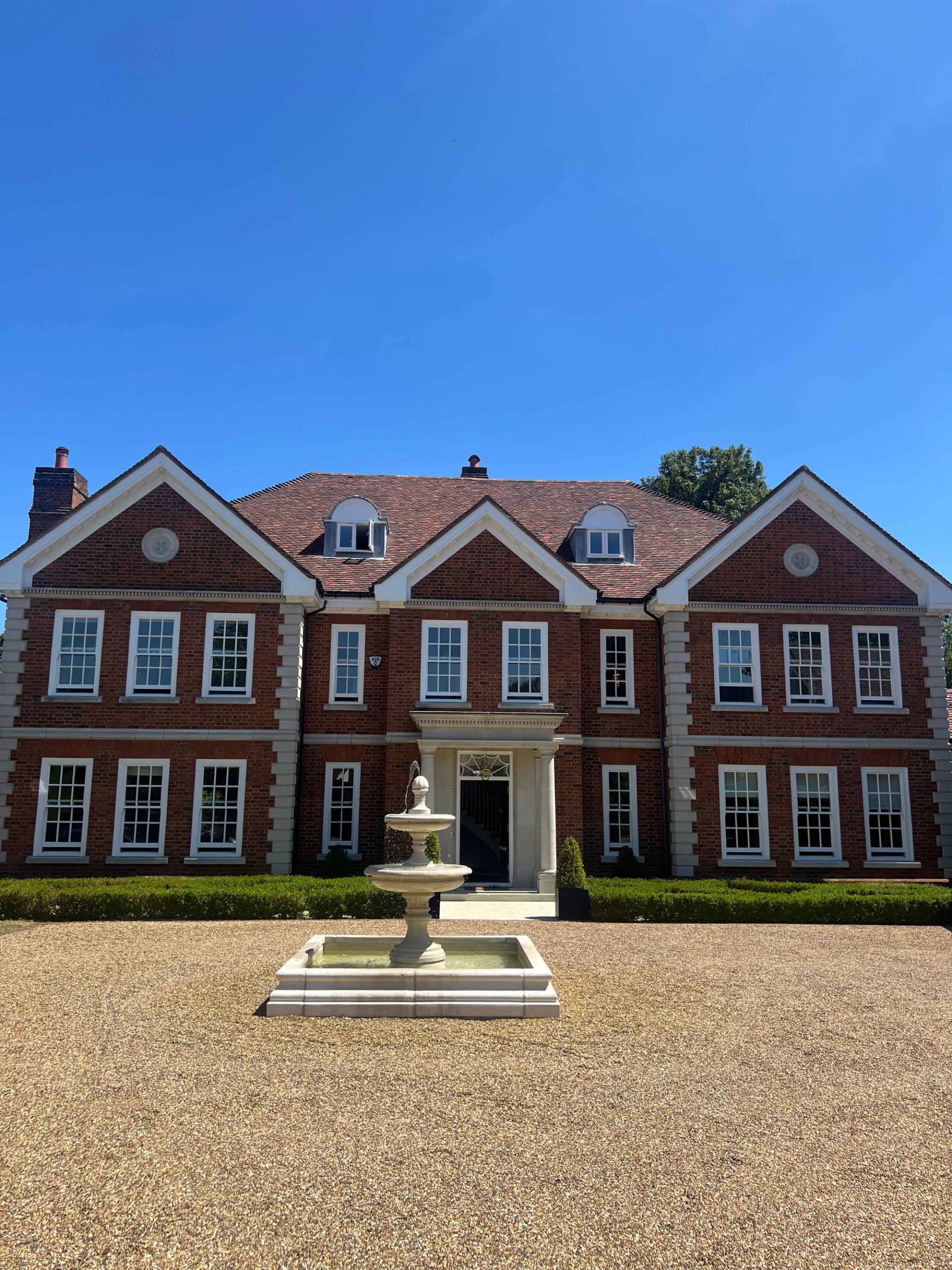 Grand Georgian-style mansion shoot location in Bromley, BR7 featuring red brick facade, fountain courtyard, and manicured hedge gardens via Love Locations.