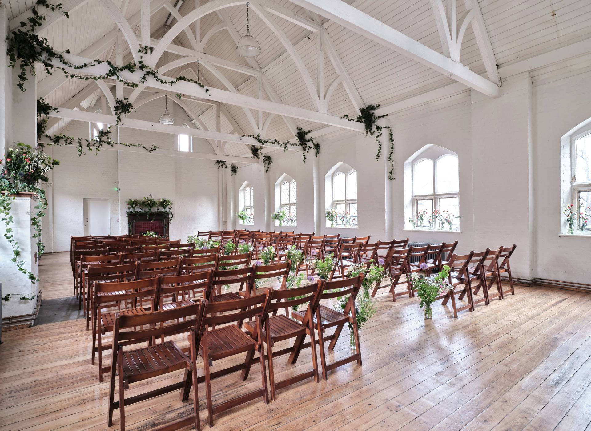 Charming wedding ceremony setup featuring rows of wooden chairs and hanging greenery along white timber beams, Love Locations.
