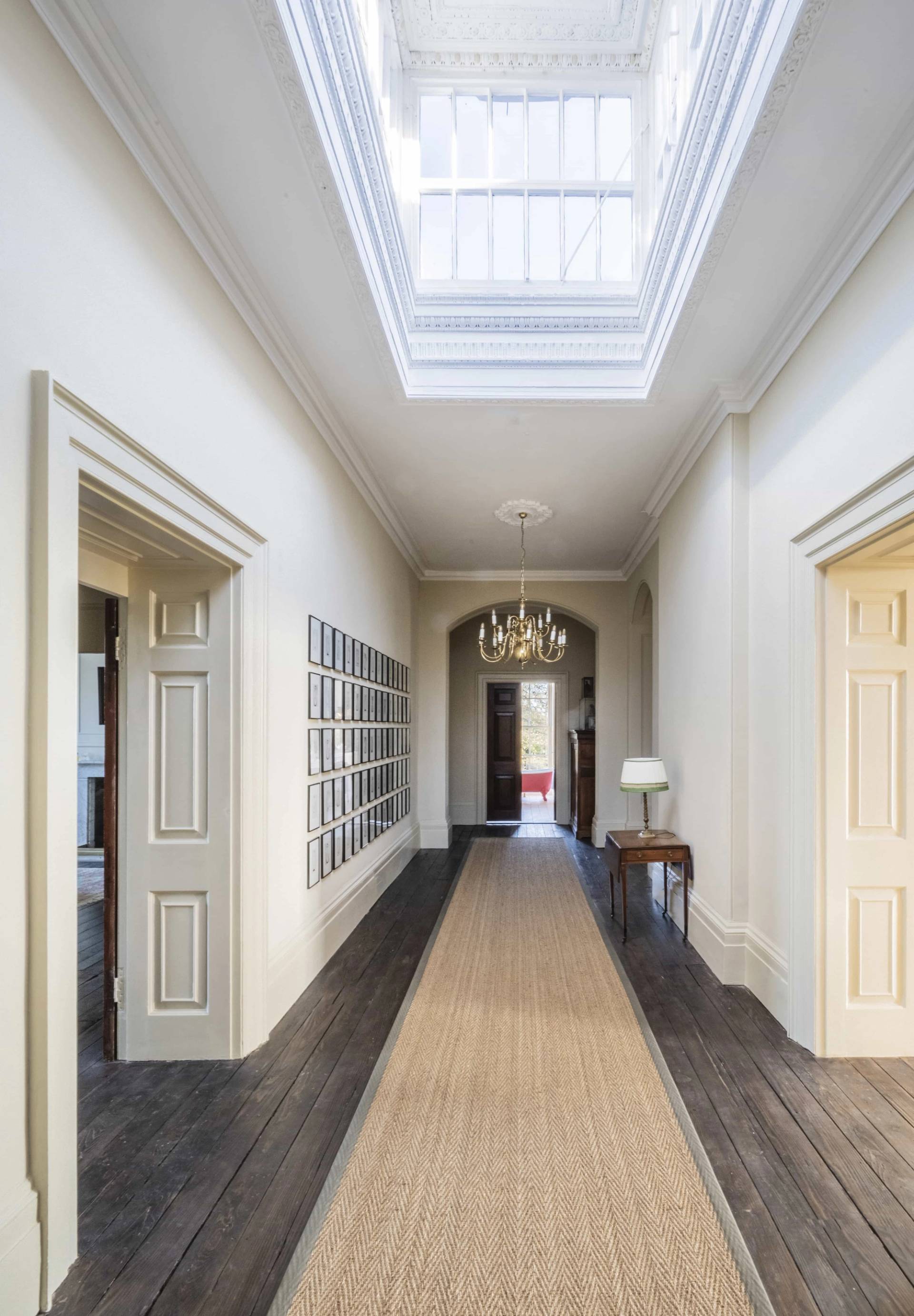 Sunlit top-floor hallway featuring a glass skylight ceiling lantern, white walls, and a picture gallery wall, perfect for fashion lookbooks, Love Locations LE7