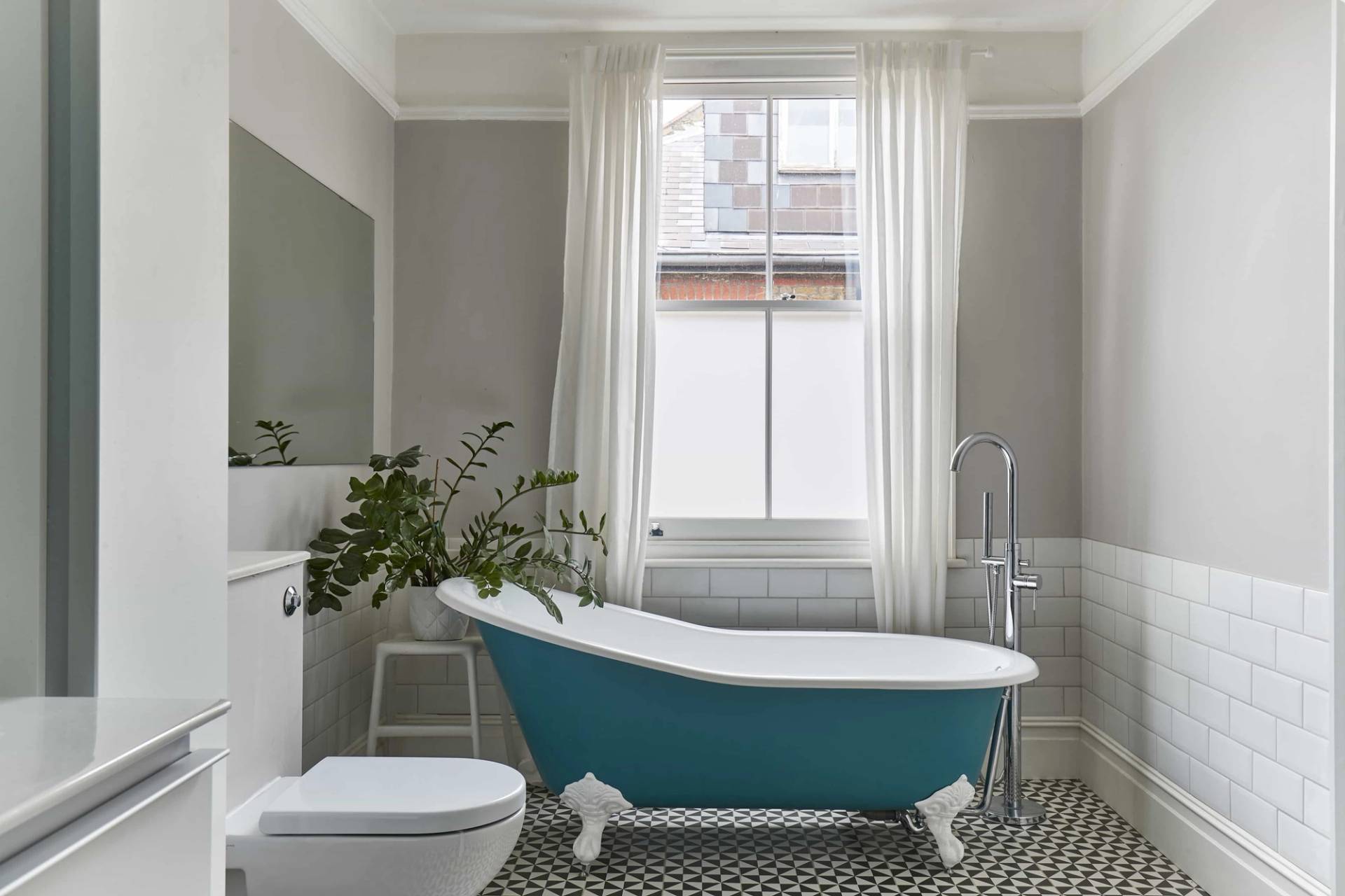 Luxury family bathroom featuring a bright teal clawfoot roll-top bathtub, white subway wall tiles, and sash window light, Love Locations.