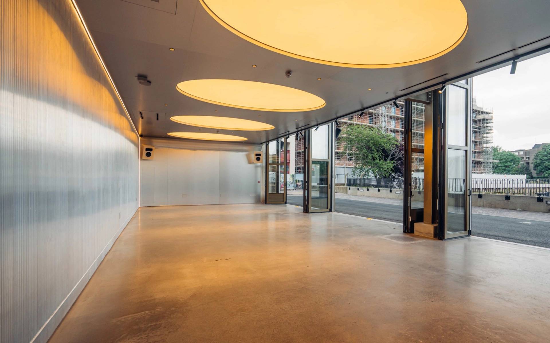 Sprawling minimalist listening bar venue for shoot hire in Brentford TW8 from Love Locations, featuring polished concrete floors and dramatic circular ceiling light panels.